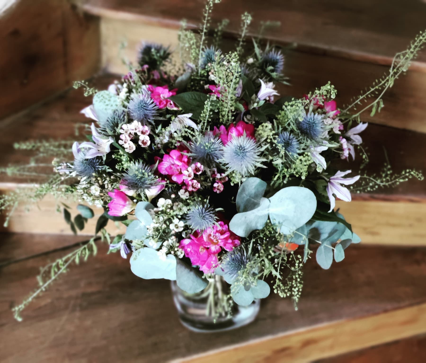 Composition champêtre mêlant chardons bleus, fleurs fuchsia et eucalyptus